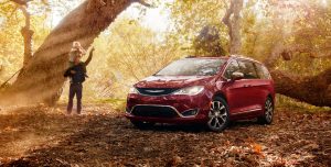 Chrysler Pacifica Hybrid in a wooded glen with a father holding his daughter on his sholders.