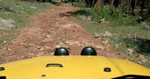 A yellow Jeep driving up a mountain trail.