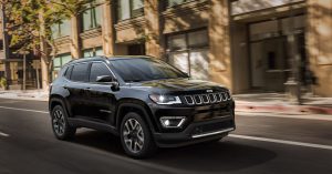 Black 2018 Jeep Compass driving down a city road.