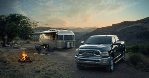 A black Ram 2500 connected to a silver Airstream camper parked beside a campfire in the mountains.