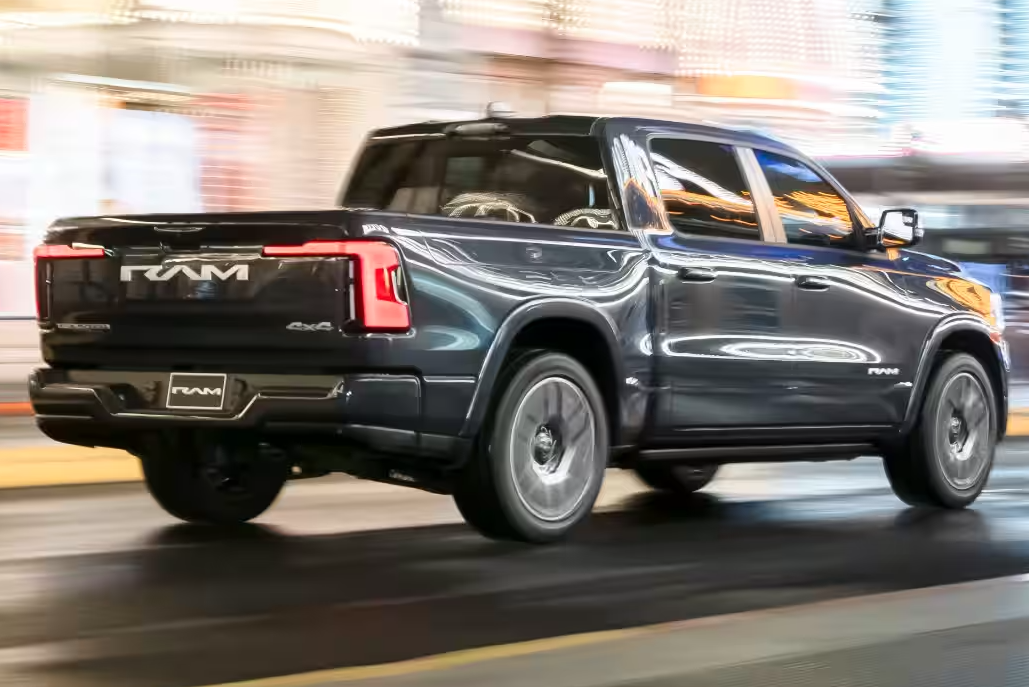 Ram 1500 REV electric truck driving at night, showcasing its distinctive taillights and "RAM" badging.